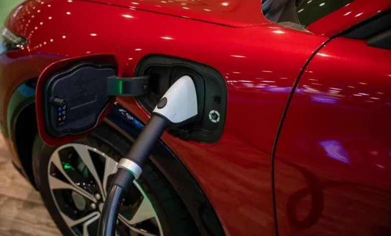 Close-up of a red electric car charging. A white charging cable is plugged into the car's charging port.
