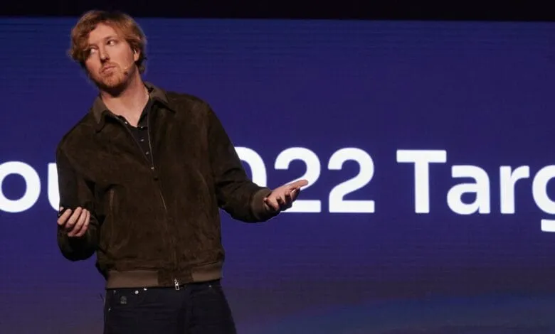 A man in a brown jacket, Austin Russell, gestures while speaking at a conference with '2022 Target' visible on a screen behind him.