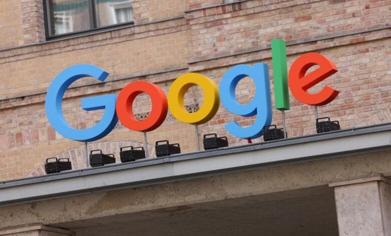 Large, colorful 3D Google logo on a building rooftop against a brick wall.