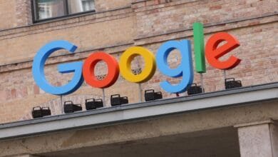 Large, colorful Google logo on a building rooftop against a brick wall.