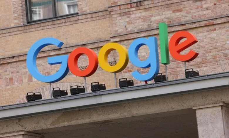 Large, colorful Google logo on a building rooftop against a brick wall.