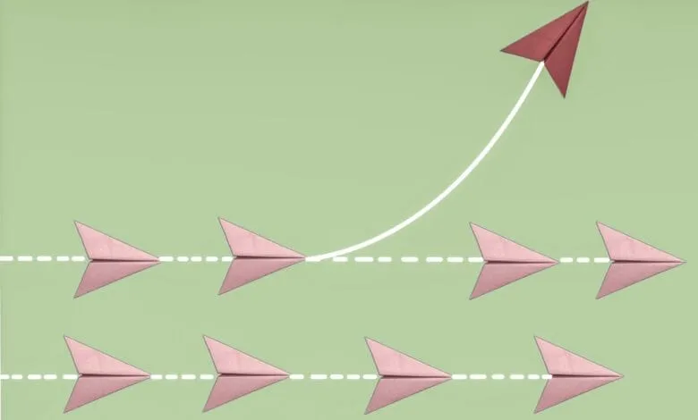 Pink paper airplanes fly in formation, one red plane soars above, diverging from the others. Illustrates breaking away from the norm.