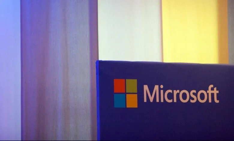Microsoft logo displayed on a purple panel against a backdrop of purple and yellow curtains.