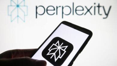 Close-up of a smartphone displaying the Perplexity AI app logo against a blurred background showing the Perplexity AI company logo.