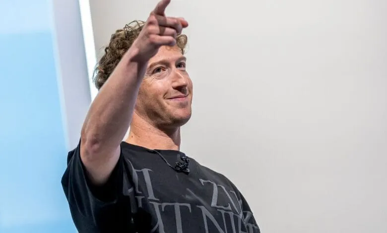 Mark Zuckerberg, in a black t-shirt, gestures with a friendly smile.