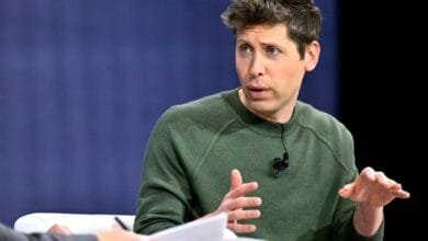 A man with brown hair in a green sweater passionately speaks, gesturing with his hands during a discussion.