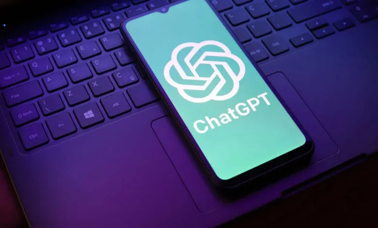Smartphone displaying the ChatGPT logo rests on a laptop keyboard, illuminated by purple and teal lighting.