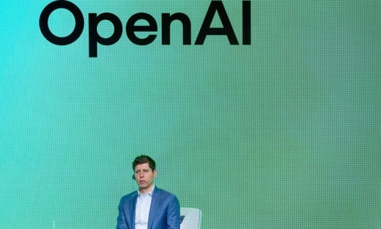 Sam Altman, OpenAI CEO, sits calmly on stage before a teal screen displaying the OpenAI logo.