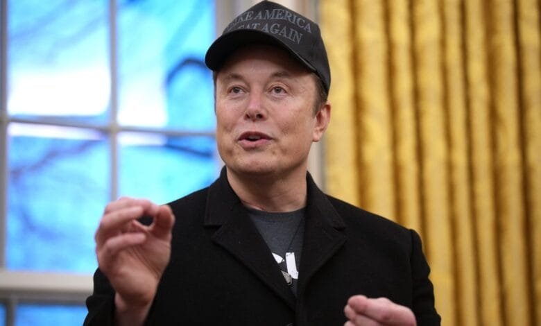 Elon Musk, wearing a black 'Make America Great Again' hat, speaks in front of a gold curtain and blue window.