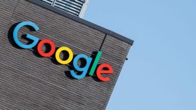 The colorful Google logo is prominently displayed on the dark brick exterior of a building against a clear blue sky.