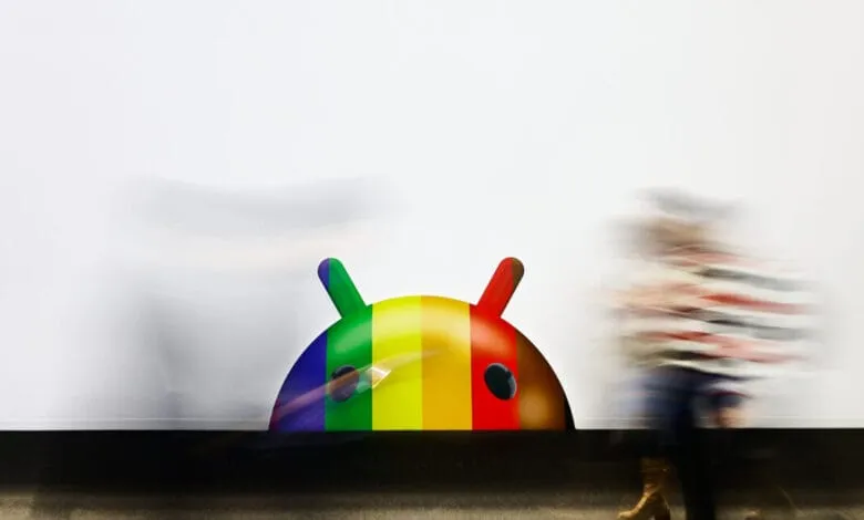A rainbow-colored Android mascot is displayed on a white wall at Mobile World Congress. Blurred figures walk past.