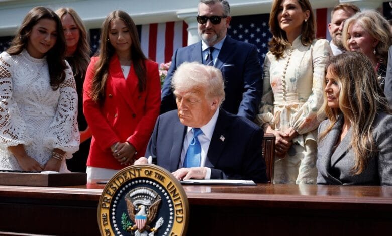 Donald Trump, former US President, signs a document at a White House ceremony, surrounded by family and staff.