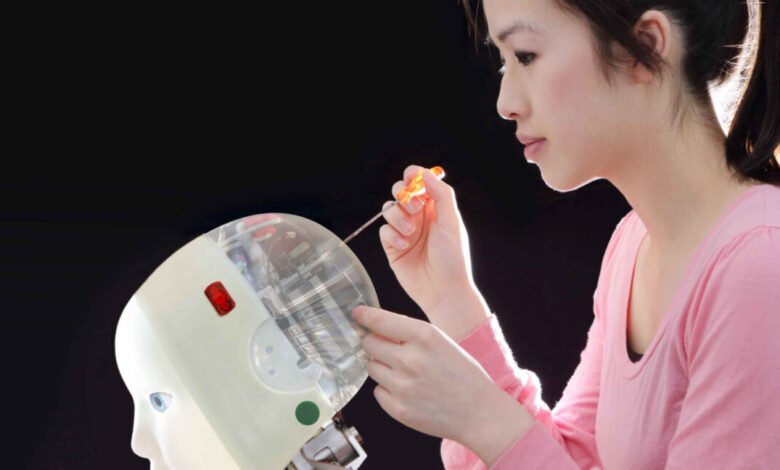 Woman in pink shirt meticulously repairs a robot's head, using a small screwdriver. The robot's internal components are visible.