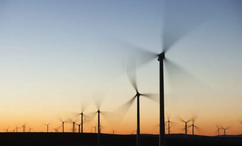 Silhouetted wind turbines spin against a vibrant sunset, showcasing clean energy production.