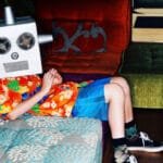 A boy sits on a couch wearing a homemade robot mask, relaxing in a colorful room.