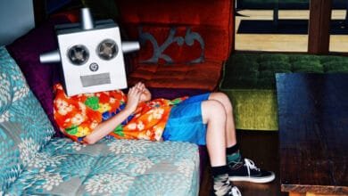 A boy sits on a couch wearing a homemade robot mask, relaxing in a colorful room.