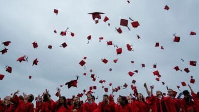 Graduates in red gowns toss their caps in the air during a joyous outdoor ceremony.
