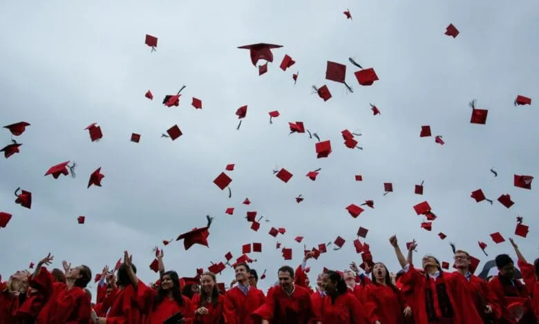 Graduates in red gowns toss their caps in the air during a joyous outdoor ceremony.