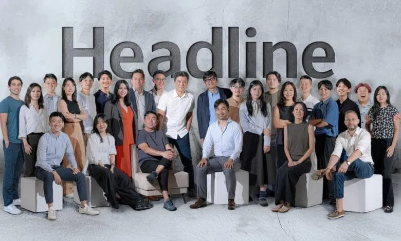 A diverse team poses for a photo in front of a large 'Headline' logo on a textured wall.