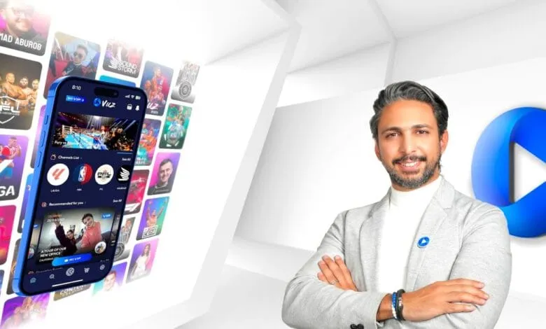 A man smiles, arms crossed, standing near a phone displaying the Vuz app, showcasing diverse sports and entertainment content.