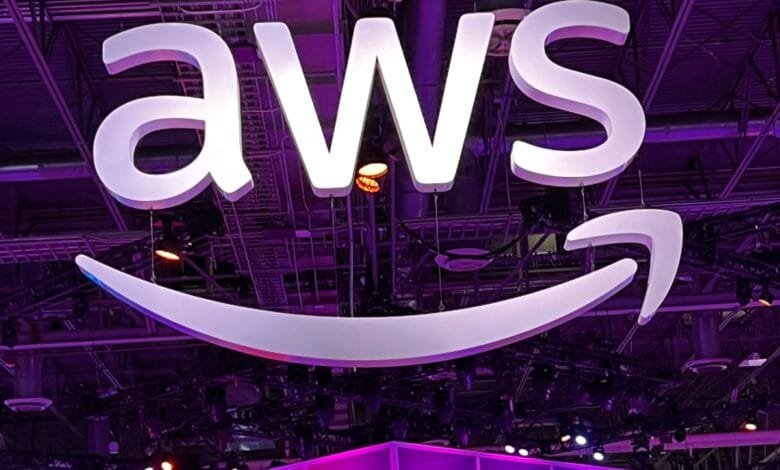 Large white AWS logo, including the Amazon smile, hangs from the ceiling of a purple-lit venue.