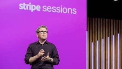 A man in glasses, John Collison, speaks at a Stripe Sessions event, a purple backdrop behind him.