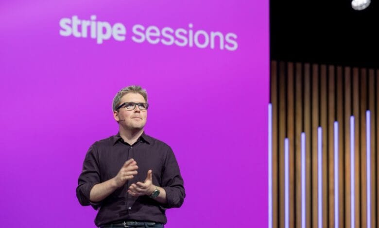 A man in glasses, John Collison, speaks at a Stripe Sessions event, a purple backdrop behind him.