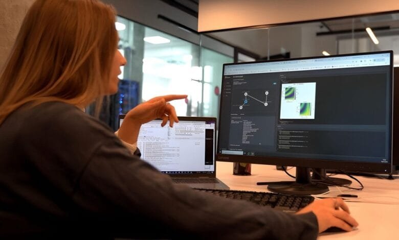 Woman points at code on a computer screen showing graphs and data visualizations. She's working at a desk with a laptop.