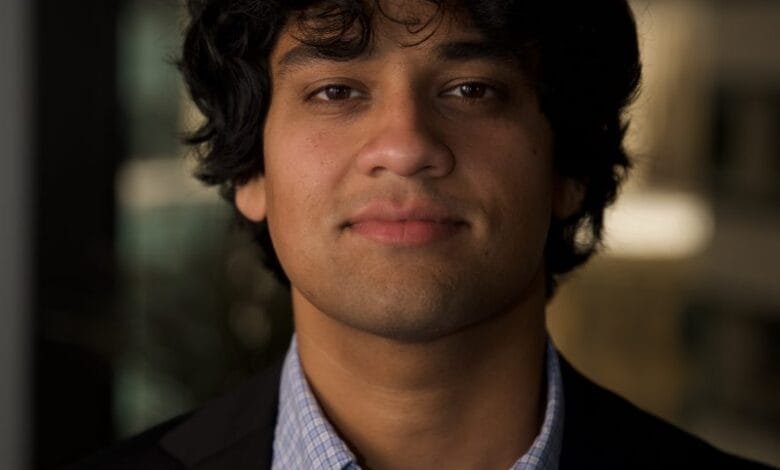 Headshot of Rahul Ligma with dark curly hair, wearing a dark suit jacket over a light blue plaid shirt.
