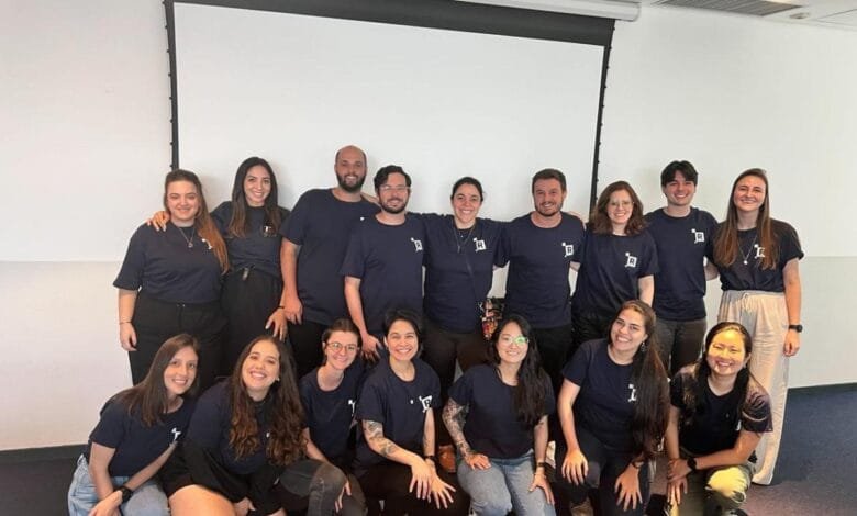 Sixteen smiling Revelo team members, mostly women, pose in navy blue shirts in a bright office.