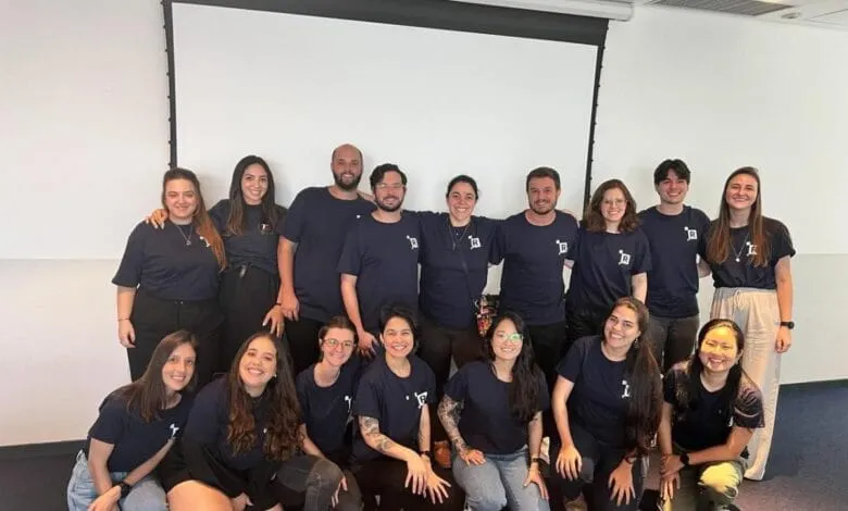 Sixteen smiling Revelo team members, mostly women, pose in navy blue shirts in a bright office.