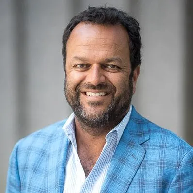Headshot of Samir Kaul, a smiling man with dark hair and beard wearing a light blue checked blazer.