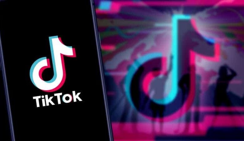 TikTok logo on a phone screen; blurred background shows dancers in pink, teal, and purple.