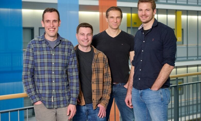 Four men, casually dressed in button-down shirts and jeans, stand together in a modern building's atrium.