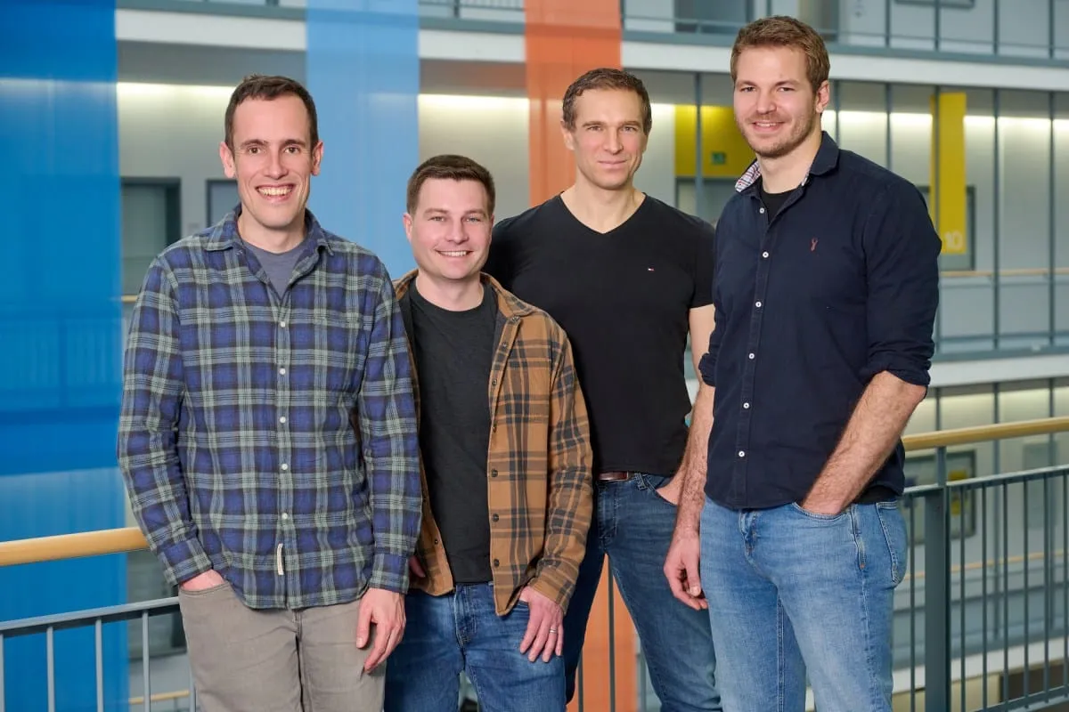 Four men, casually dressed in button-down shirts and jeans, stand together in a modern building's atrium.