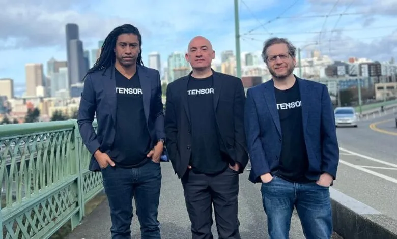 Three men in blazers and Tensor t-shirts stand on a bridge with a city skyline in the background.