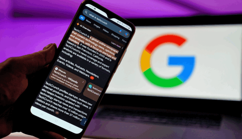 Smartphone displays TechCrunch's Wikipedia entry; blurred Google logo in background.