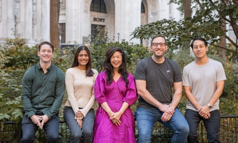 Five smiling colleagues sit on a fence in a city park, a building with 'SONY' visible in the background.