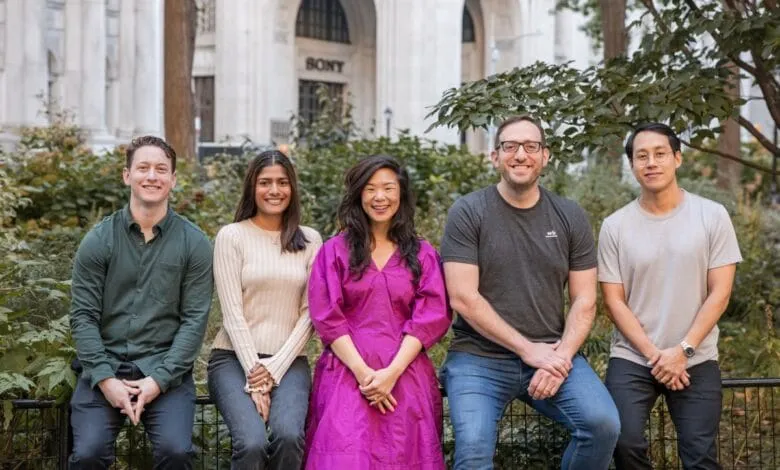 Five smiling colleagues sit on a fence in a city park, a building with 'SONY' visible in the background.
