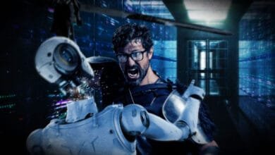 A man in futuristic armor battles a robot in a server room, sparks flying as he destroys its head.