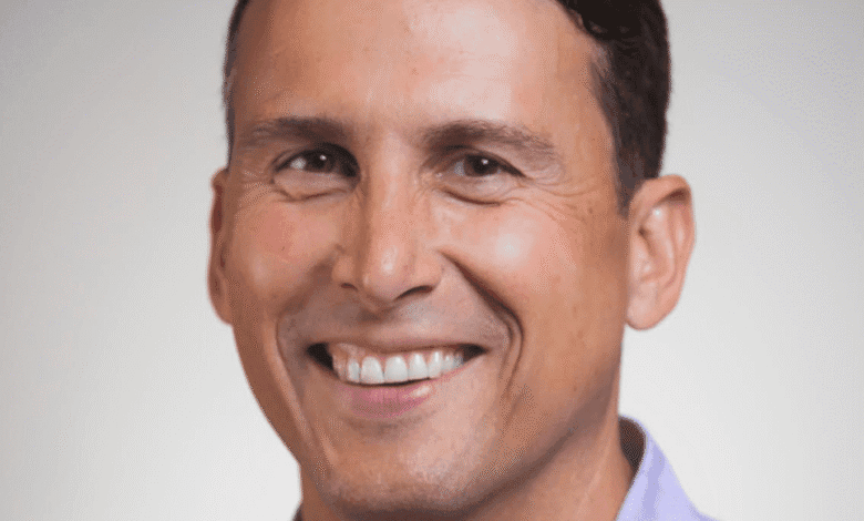 Headshot of Alex Bard, smiling warmly against a light gray background, wearing a lavender shirt.