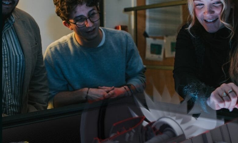 Three people collaborate, examining a detailed 3D model of a jet engine on a large screen.