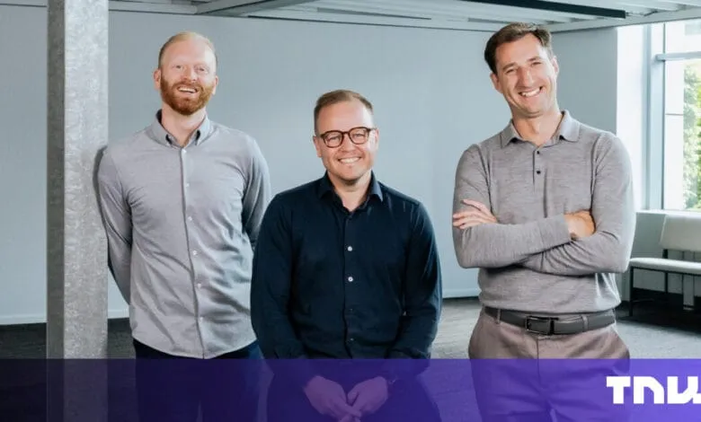 Three smiling men in business casual attire stand in a modern office.