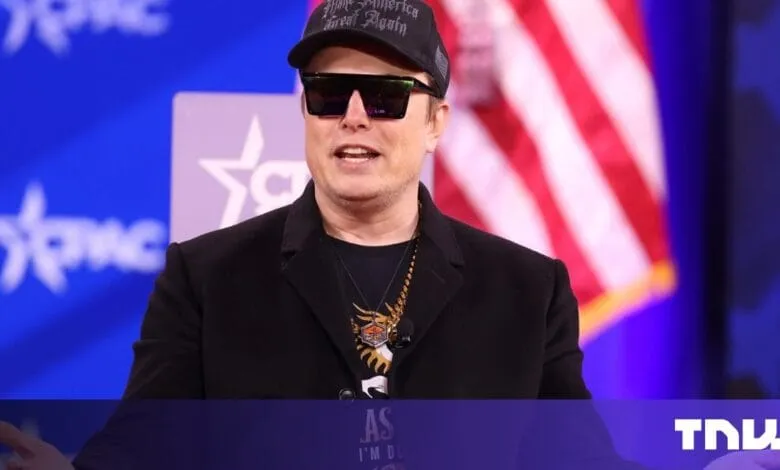 Kid Rock, wearing sunglasses and a hat, speaks at an event with an American flag in the background.