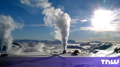 Geothermal power plant in a snowy landscape, steam rising against a bright blue sky.