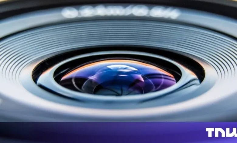 Close-up of a camera lens, showcasing its intricate design and reflective surface with blue and purple hues.