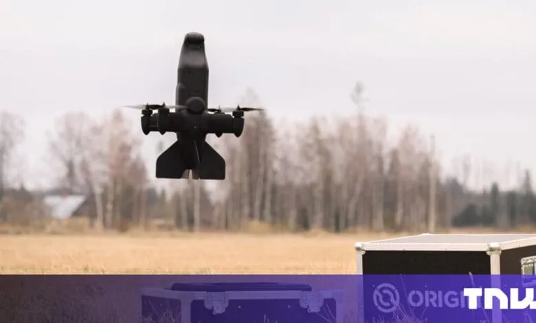 Black drone in flight over a field, approaching a dark-colored transport case.