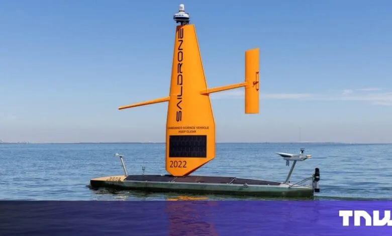 Orange SailDrone unmanned science vehicle floats on calm blue water under a clear sky.