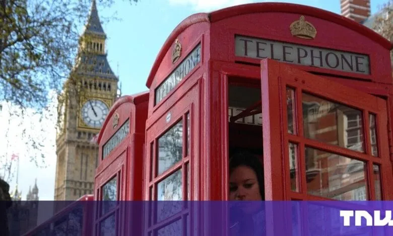 A person stands inside a red telephone booth in London, with Big Ben visible in the background.