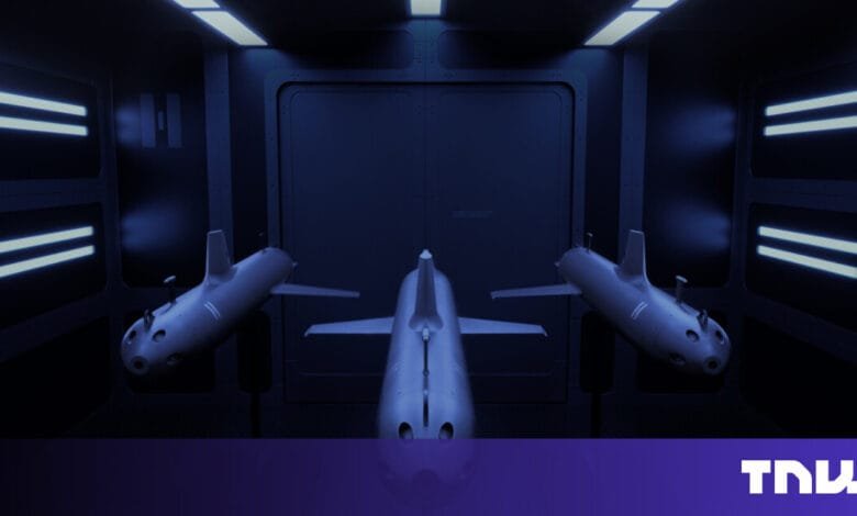 Three futuristic submarines in a dark, metallic hangar, illuminated by bright blue lights.